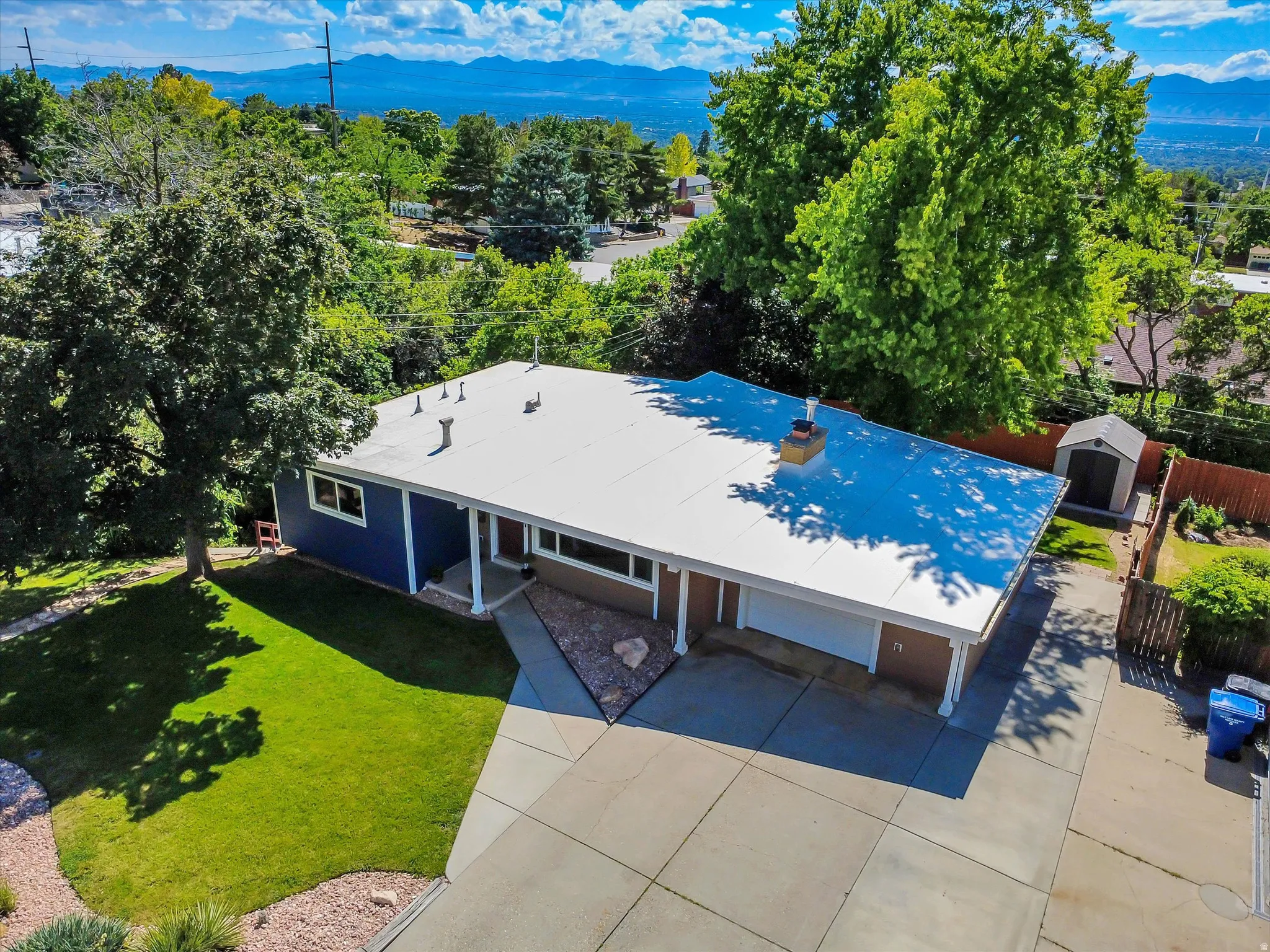 Ranch-style residence featuring a blue and brown exterior, an expansive concrete driveway, and a white flat roof