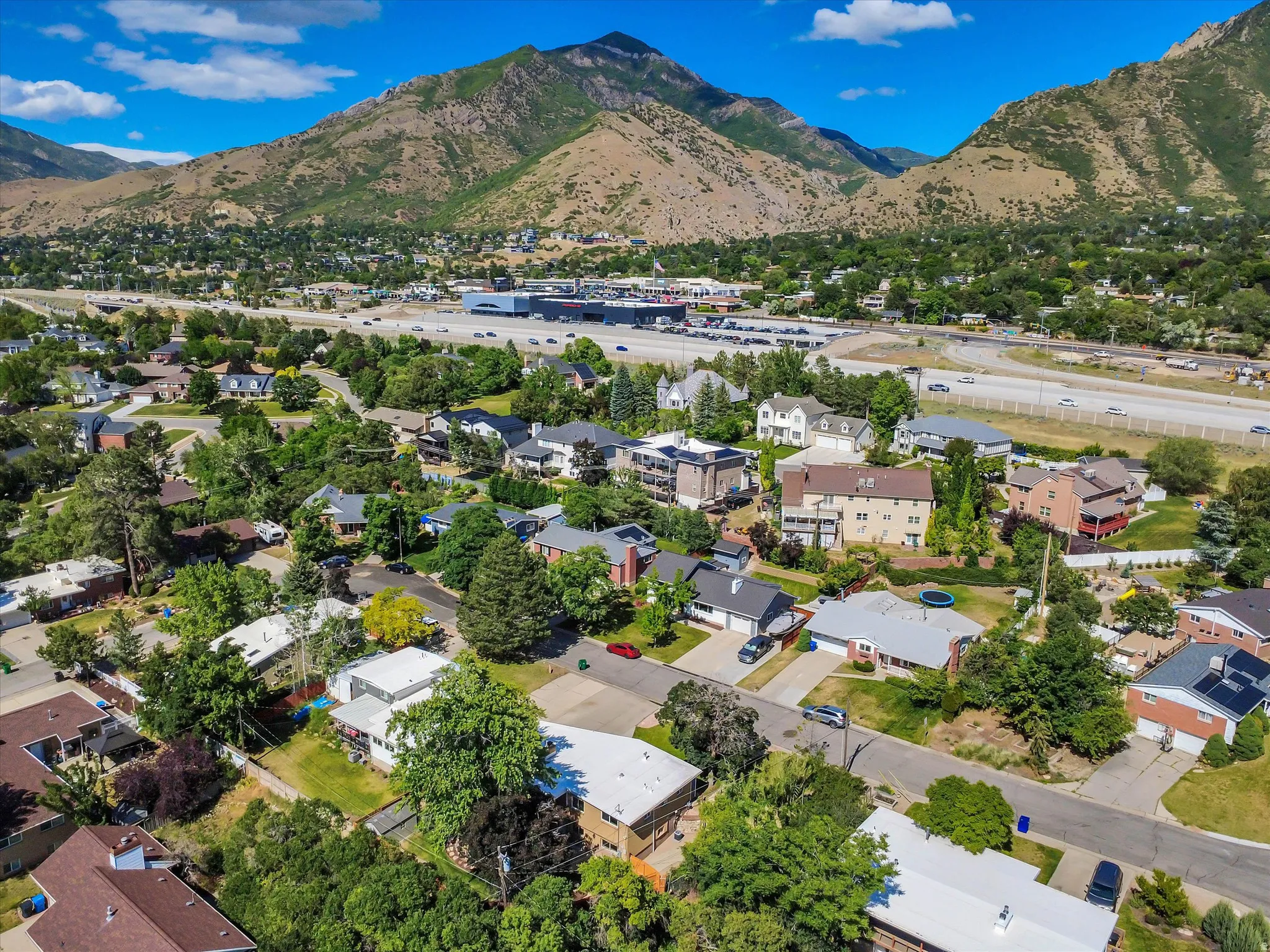 Expansive neighborhood situated against a dramatic mountain backdrop, featuring a mix of residential properties with mature landscaping and convenient highway access