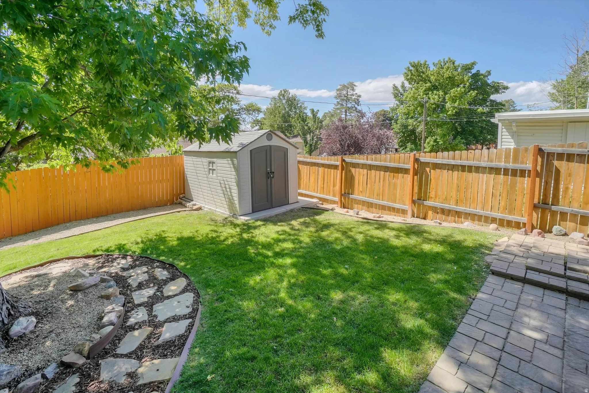 Expansive backyard featuring a lush lawn, a beige storage shed, and a stone-paver patio