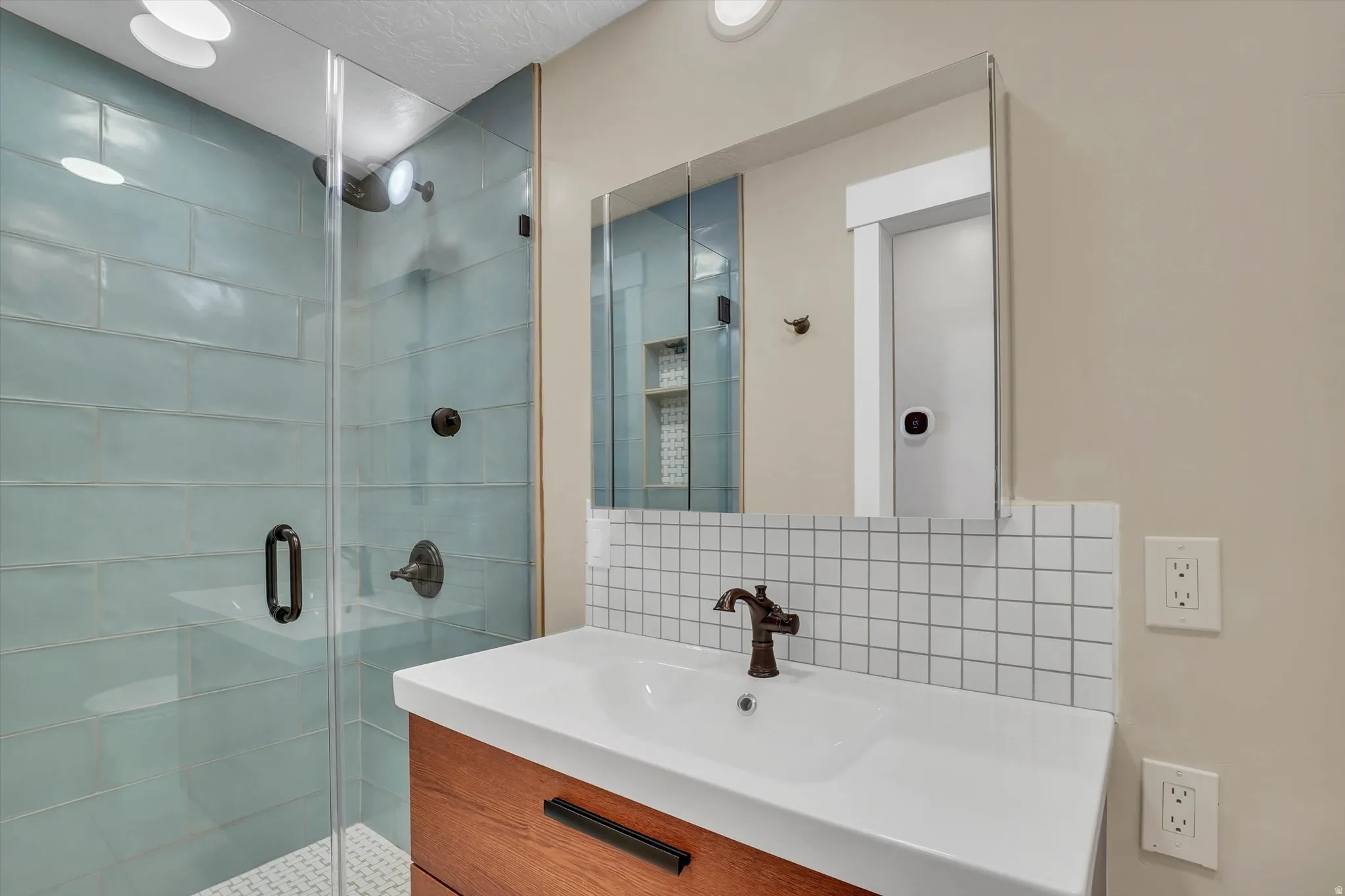 Full bathroom featuring a glass-enclosed shower with subway tile, a vanity with wood-finish cabinetry, a white countertop with integrated sink, and an overhead mirrored medicine cabinet