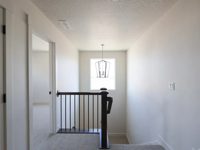 Upper level landing featuring light gray carpeting, a dark wood newel post with black metal balusters, a rectangular window, and a hanging lantern-style light fixture