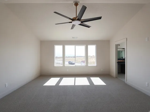 Vaulted ceiling with an attached ceiling fan, large windows, and neutral carpeting, spacious primary bedroom