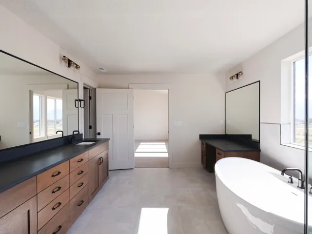 Dual vanity with dark countertops and integrated sinks, a freestanding soaking tub, large rectangular wall mirrors, and light tile flooring, big primary bathroom , conected to laundry and an ample walk in closet