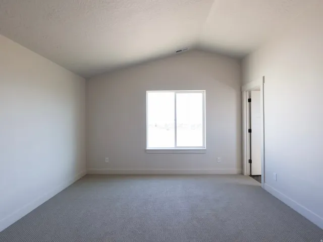 Vaulted ceiling with a window, light gray carpet flooring, and white trim.Guest bedroom with attached bathroom