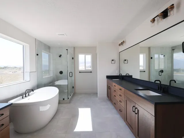 Freestanding soaking tub, glass-enclosed shower, dual wood-finish vanities with dark countertops, and matte black fixtures, bi shower and linen closet.