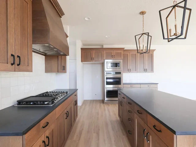 Wood-finish cabinetry with dark countertops, built-in stainless steel appliances, and wood-finish flooring