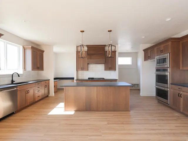 Kitchen featuring wood-finish flooring, a central island with countertop, coordinating wood cabinetry, stainless steel appliances, and pendant lighting