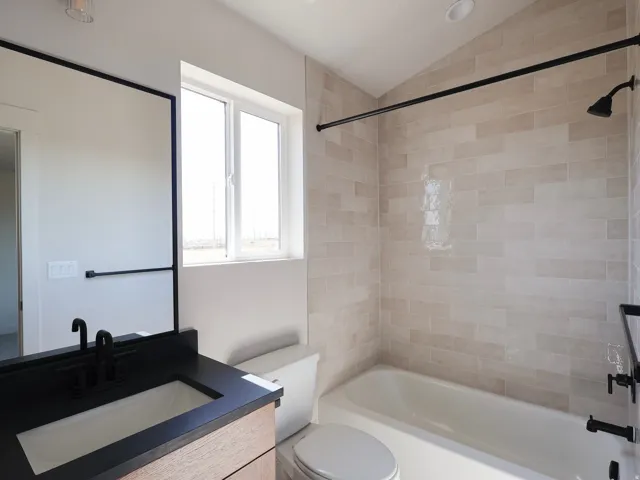 Bathroom featuring a wood-finish vanity, dark countertop, rectangular undermount sink, and matte black fixtures