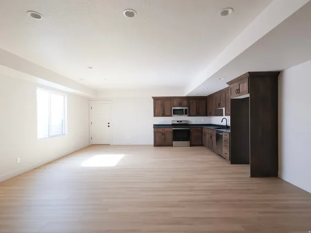 Open concept living space featuring wood-finish flooring, recessed lighting, and a kitchen with dark wood cabinetry, dark countertops, and stainless steel appliances