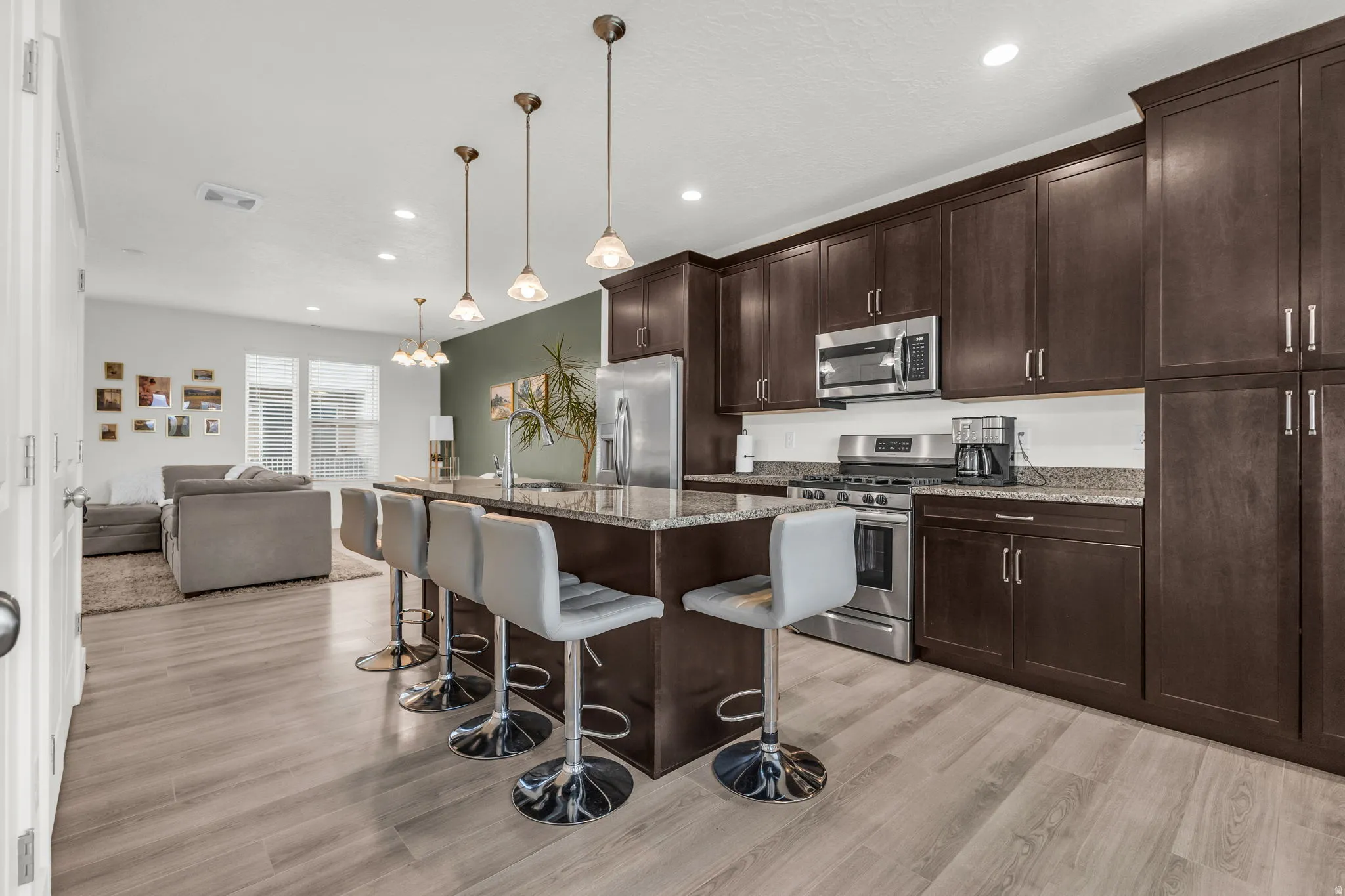 Open-concept kitchen featuring dark wood cabinetry, stainless steel appliances, granite countertops, and a large island with pendant lighting