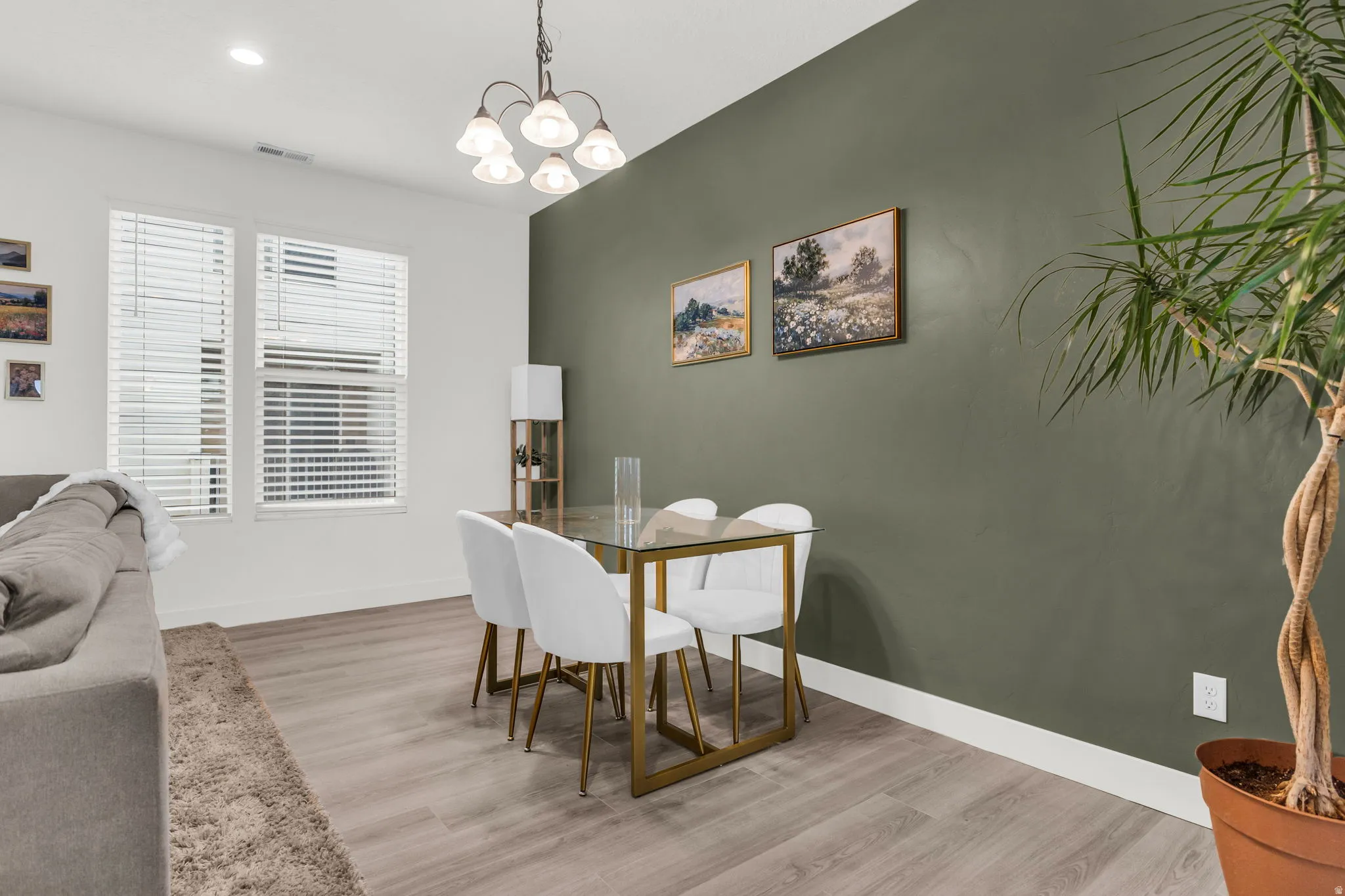 Open-concept living space featuring wood-finish flooring, a contemporary chandelier, multiple windows with blinds, and a distinctive accent wall