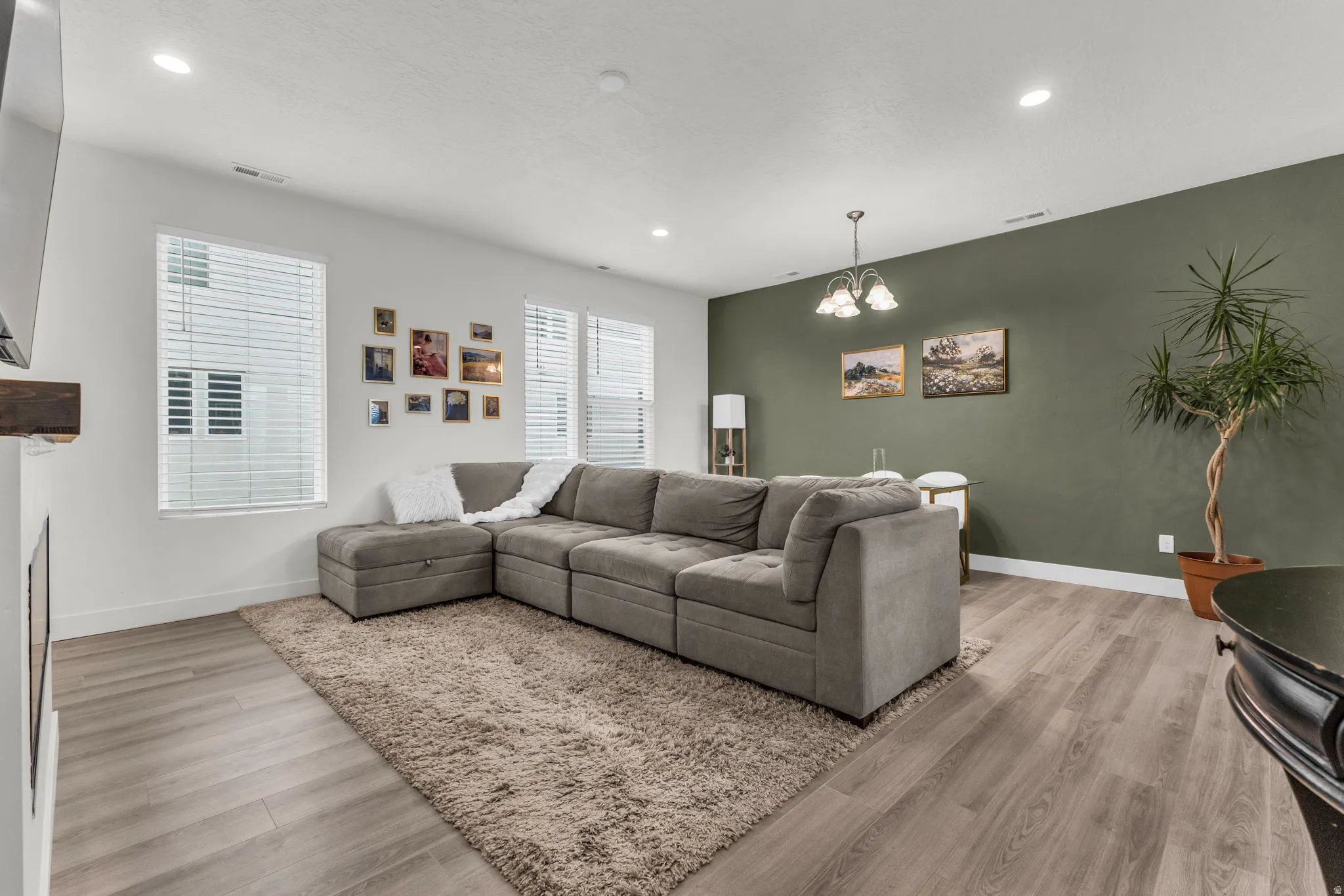 Open-concept living area featuring wood-finish flooring, recessed lighting, and multiple windows with blinds