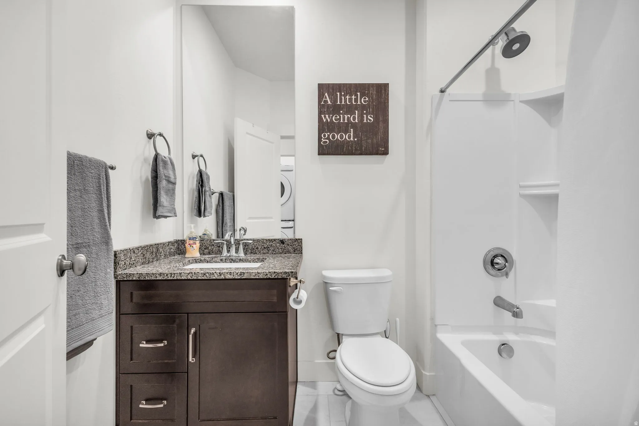 Bathroom featuring a dark wood-finish vanity with a stone countertop, a white toilet, and a white shower-over-tub unit