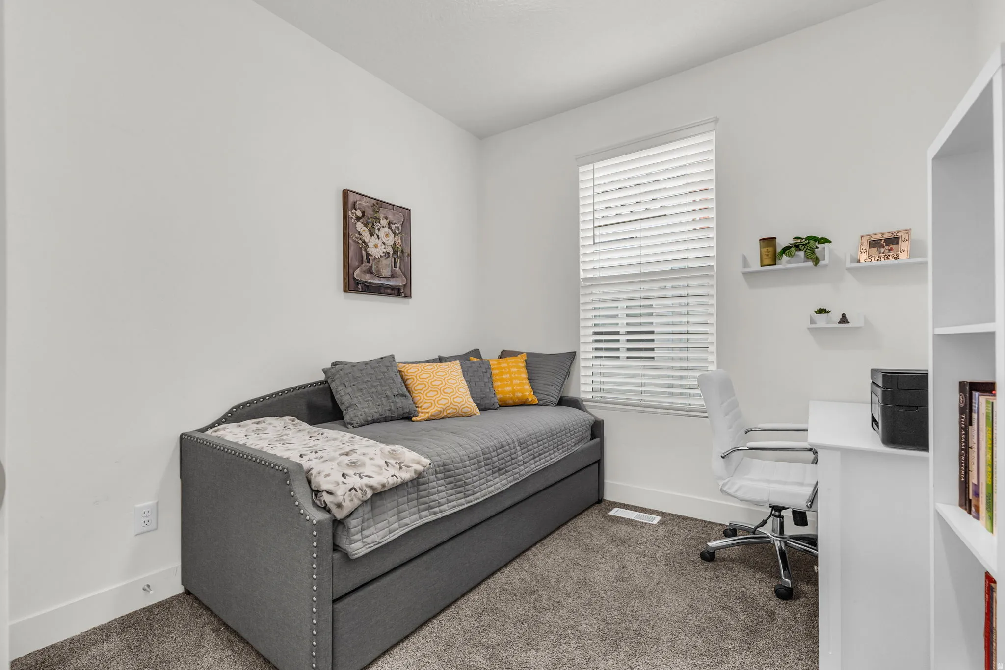 Bright room featuring white walls, textured carpeting, a single window with blinds, and white floating shelves