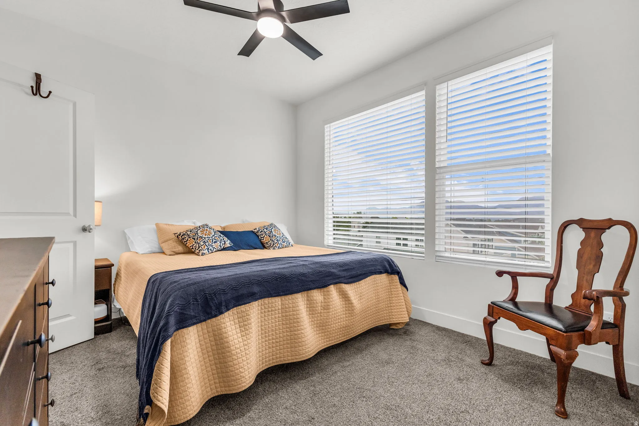 Bedroom featuring a ceiling fan, two large windows with horizontal blinds, neutral wall paint, and gray carpet flooring