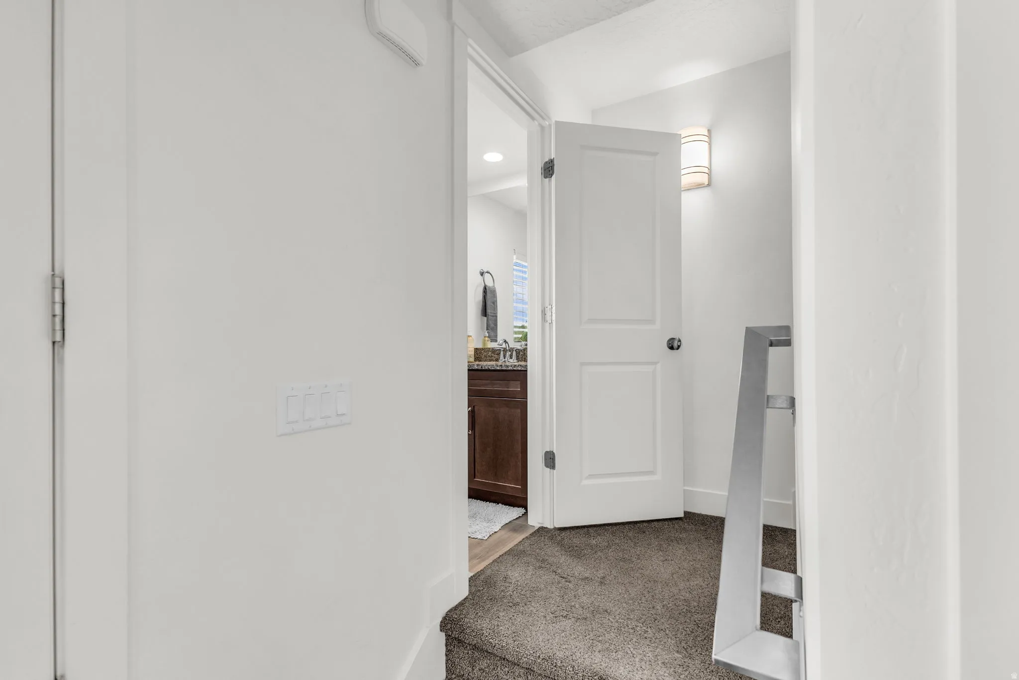 Carpeted hallway featuring a contemporary wall sconce, white interior doors, and a modern metal stair railing