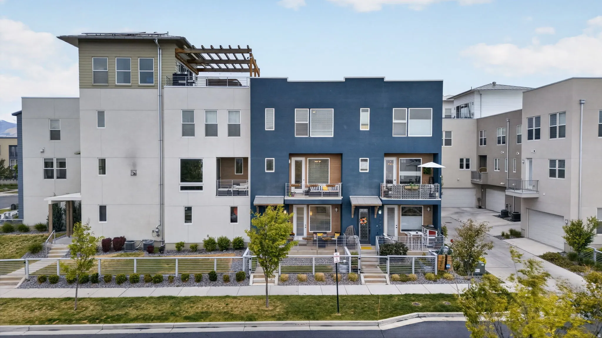 Modern multi-level exterior featuring varied facades in white and deep blue, multiple balconies with glass railings, and a prominent rooftop pergola structure