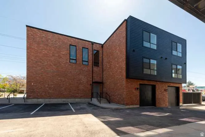 Modern exterior featuring a brick facade with dark siding accents, multiple windows, and two garage doors