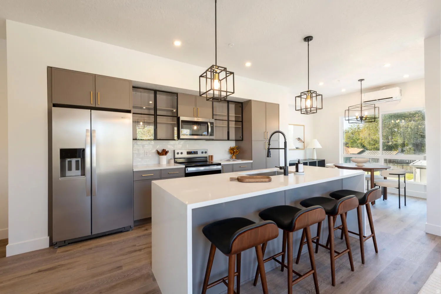 Open-concept kitchen featuring an oversized island with seating, stainless steel appliances, modern cabinetry with glass accents, and wood-finish flooring