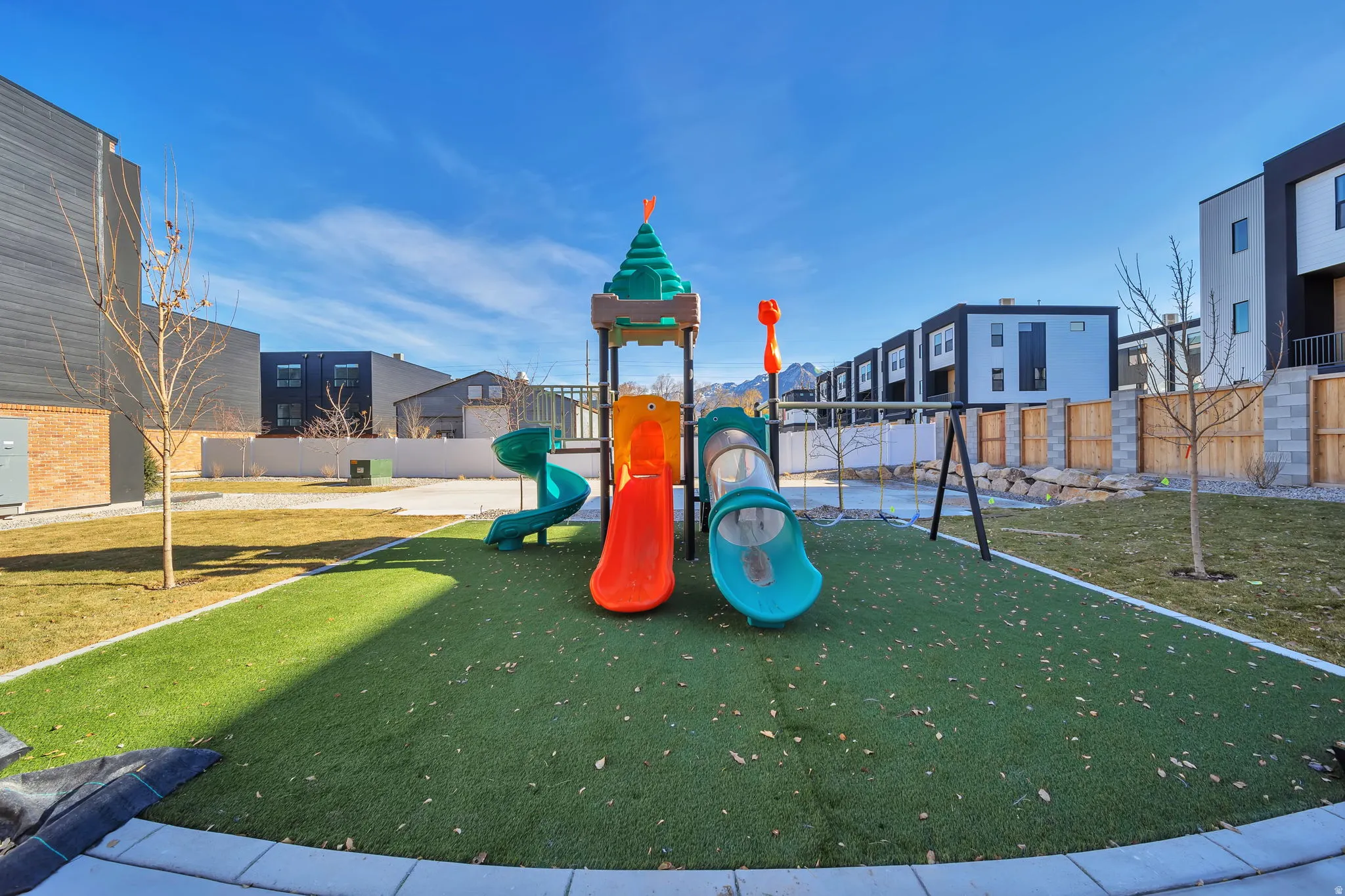 Community recreational area featuring artificial turf, a multi-slide play structure, and swing set