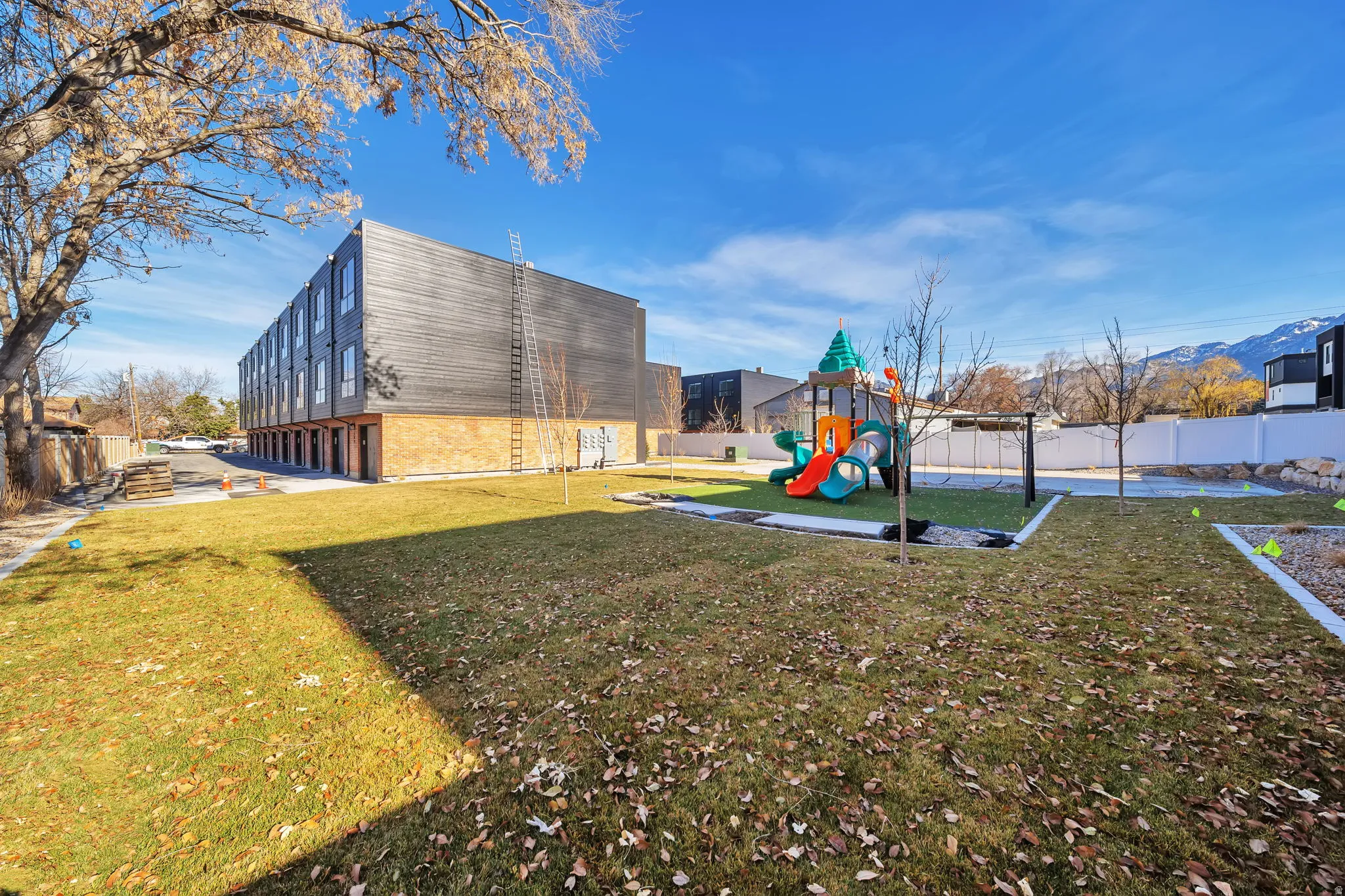 Expansive grassy yard area with a vibrant playground structure featuring slides and swings