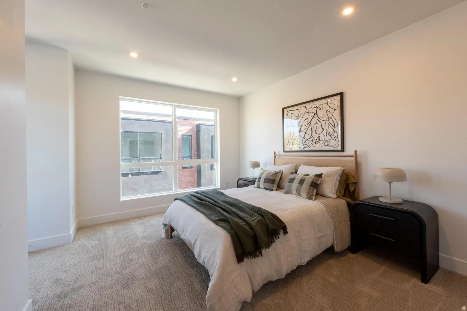 Bedroom featuring a large multi-pane window, recessed lighting, neutral carpeting, white baseboards, and a light wood-finish headboard