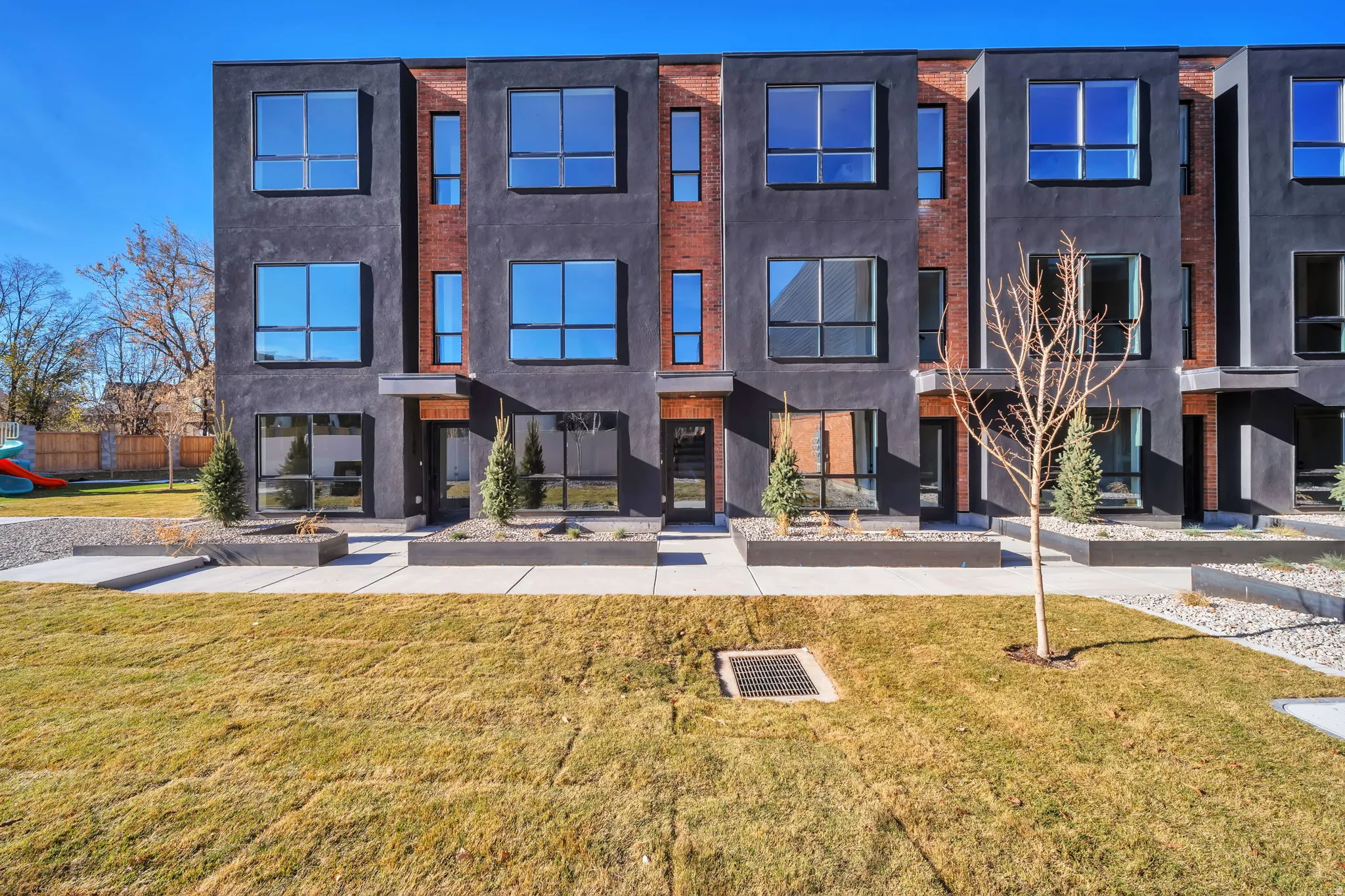 Contemporary townhome facade featuring dark stucco and brick accents