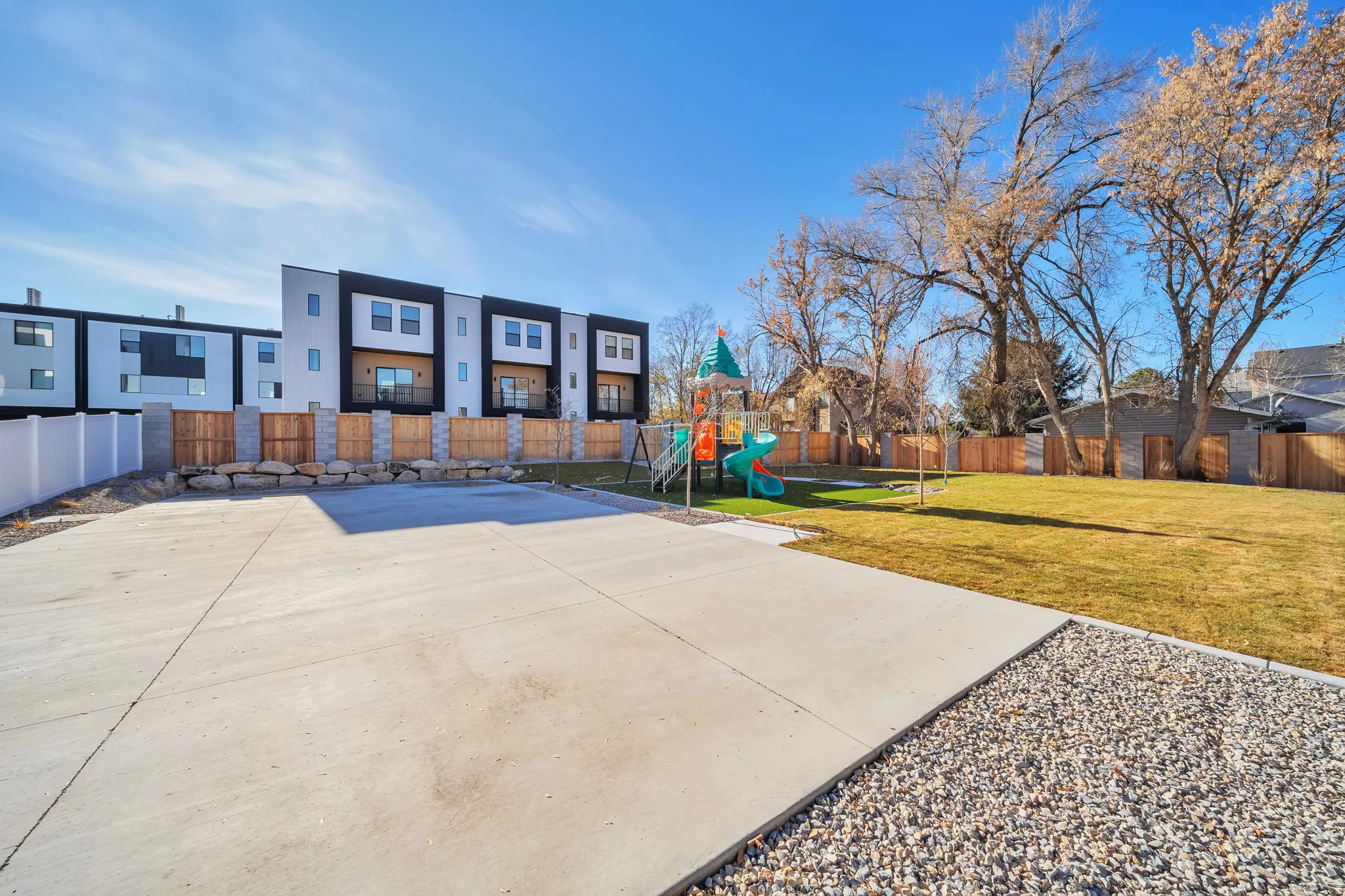 Expansive concrete paved area bordered by decorative gravel and a natural wood fence