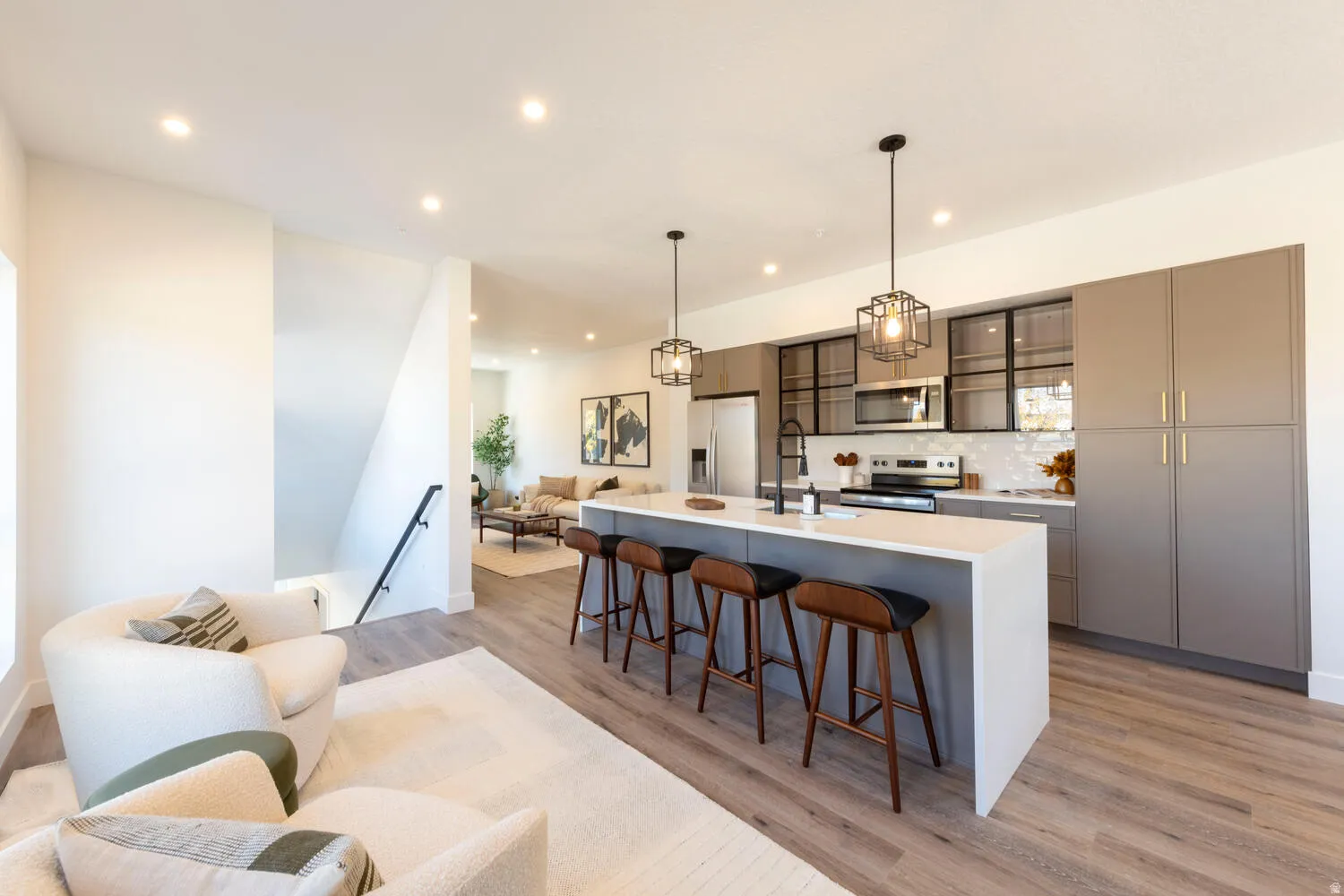 Modern kitchen featuring a large island with seating, stainless steel appliances, contemporary pendant lighting, and ample cabinetry with glass-front accents