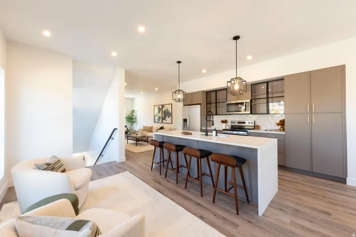 Modern kitchen featuring a large island with seating, stainless steel appliances, contemporary pendant lighting, and ample cabinetry with glass-front accents