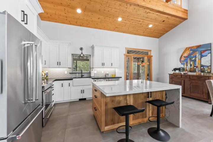 Kitchen featuring a large center island with a waterfall-edge countertop, white shaker-style cabinetry, stainless steel appliances, and wood-finish vaulted ceilings
