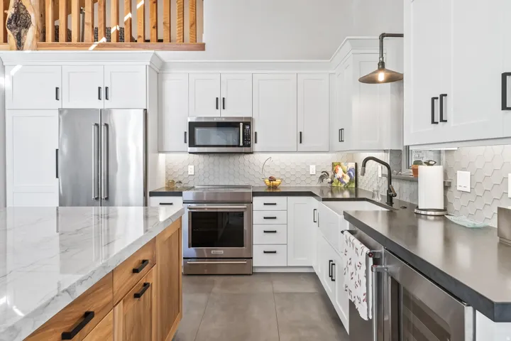 Modern kitchen featuring white shaker cabinetry and a light wood-finish island with a stone countertop