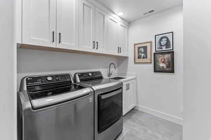 Dedicated laundry space featuring white shaker cabinetry, an integrated sink with a stainless steel faucet, and light grey countertop