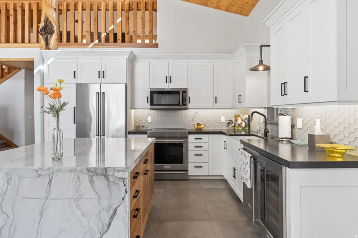 Gourmet kitchen featuring a waterfall island with a stone countertop, white shaker cabinetry, stainless steel appliances, a hexagonal tile backsplash, and a beverage refrigerator