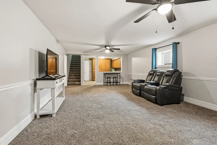Spacious carpeted room featuring light gray walls with white wainscoting, recessed lighting, and dual ceiling fans