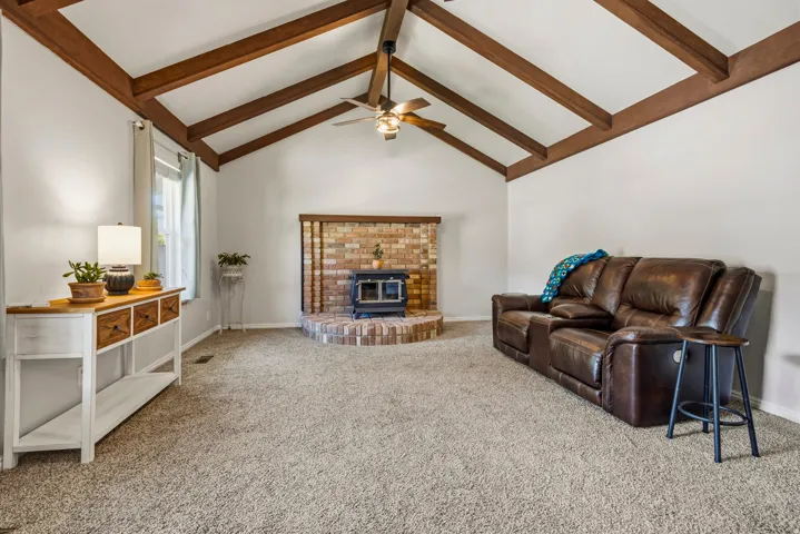 Living area featuring a vaulted ceiling with exposed wood beams, a ceiling fan, and light-toned wall finishes