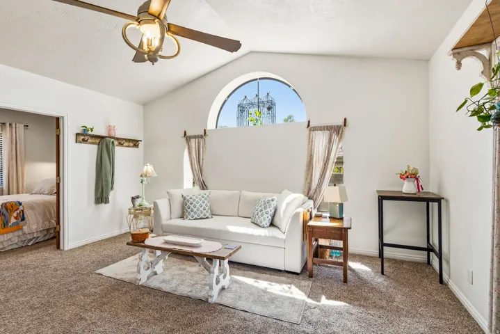Vaulted ceiling with a ceiling fan, arched window, and wall-mounted coat rack