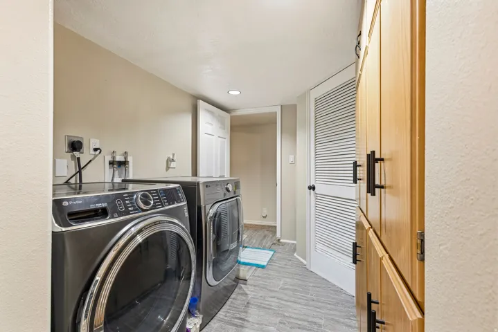 Dedicated laundry area with light wood-finish cabinetry, black hardware, and gray wood-look flooring