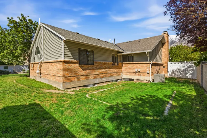 Rear exterior featuring a brick and siding facade, a gabled roofline, a visible chimney, and a fenced perimeter