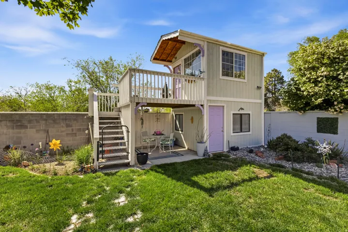 Two-story auxiliary structure featuring a ground-level patio, an upper-level balcony with white railings, and a distinct lavender entry door