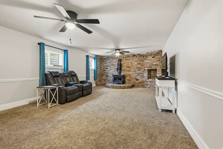 Carpeted room featuring a brick accent wall with a built-in wood-burning stove and a brick hearth