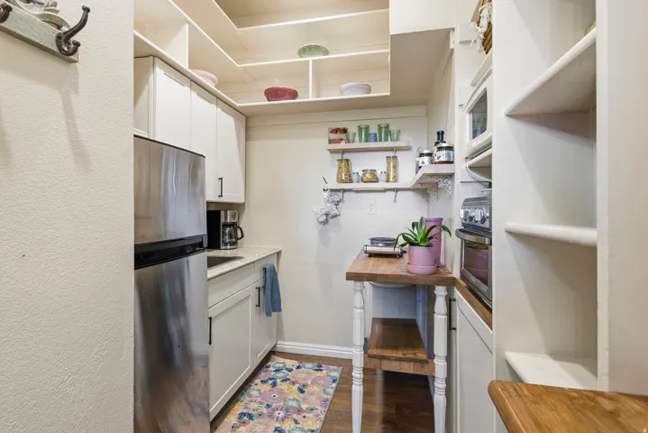 Compact kitchen featuring stainless steel refrigerator, white cabinetry with dark hardware, a light-toned countertop, and wood-finish flooring