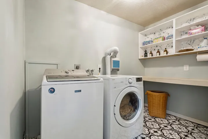 Dedicated laundry space featuring patterned floor tile, light-colored walls, built-in shelving, and a wood-finish countertop