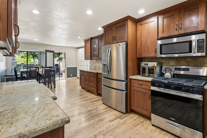 Kitchen featuring wood-finish flooring, wood cabinetry, granite countertops, and stainless steel appliances including a refrigerator, microwave, and range