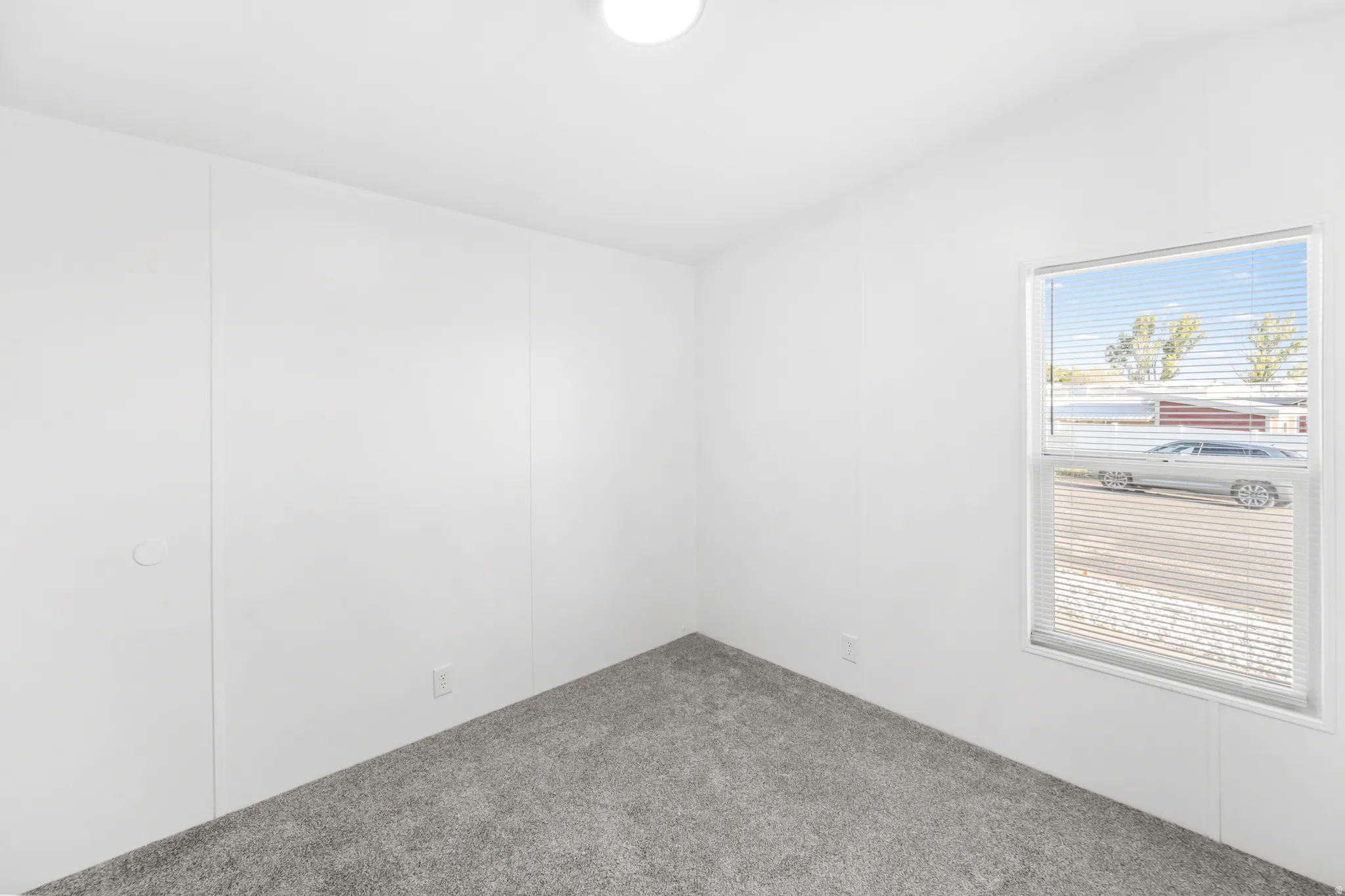 Bright room featuring white walls, gray textured carpeting, and a window with horizontal blinds