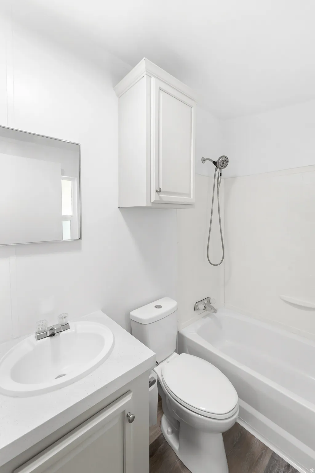 White bathroom featuring a single vanity, undermount sink, wall-mounted mirror, and white cabinetry