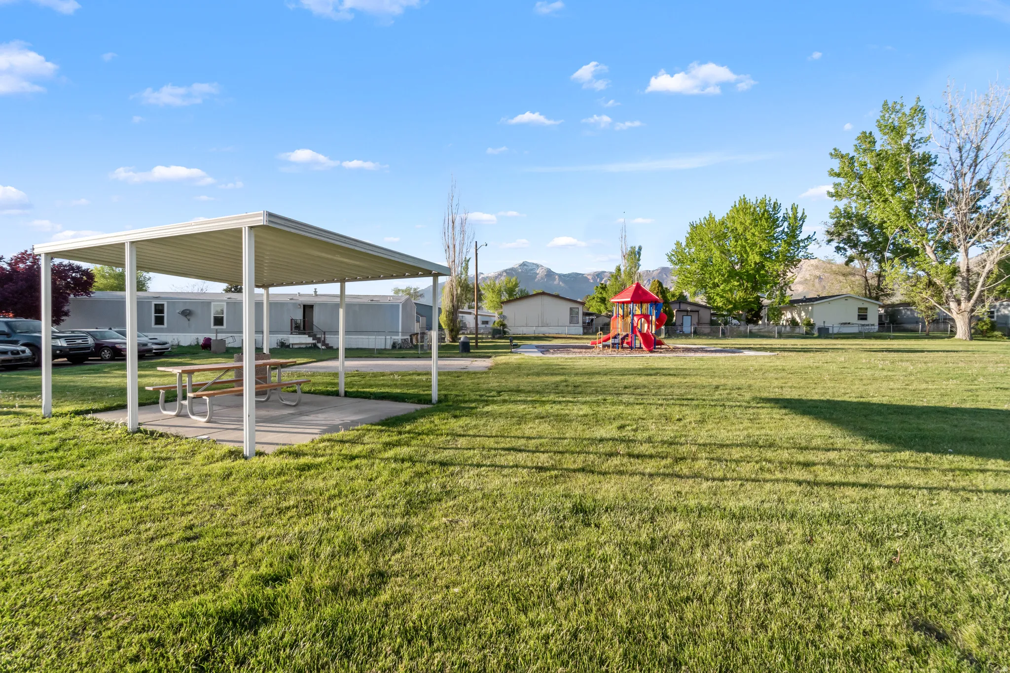 Expansive green space featuring a covered picnic area with a concrete pad and a playground structure