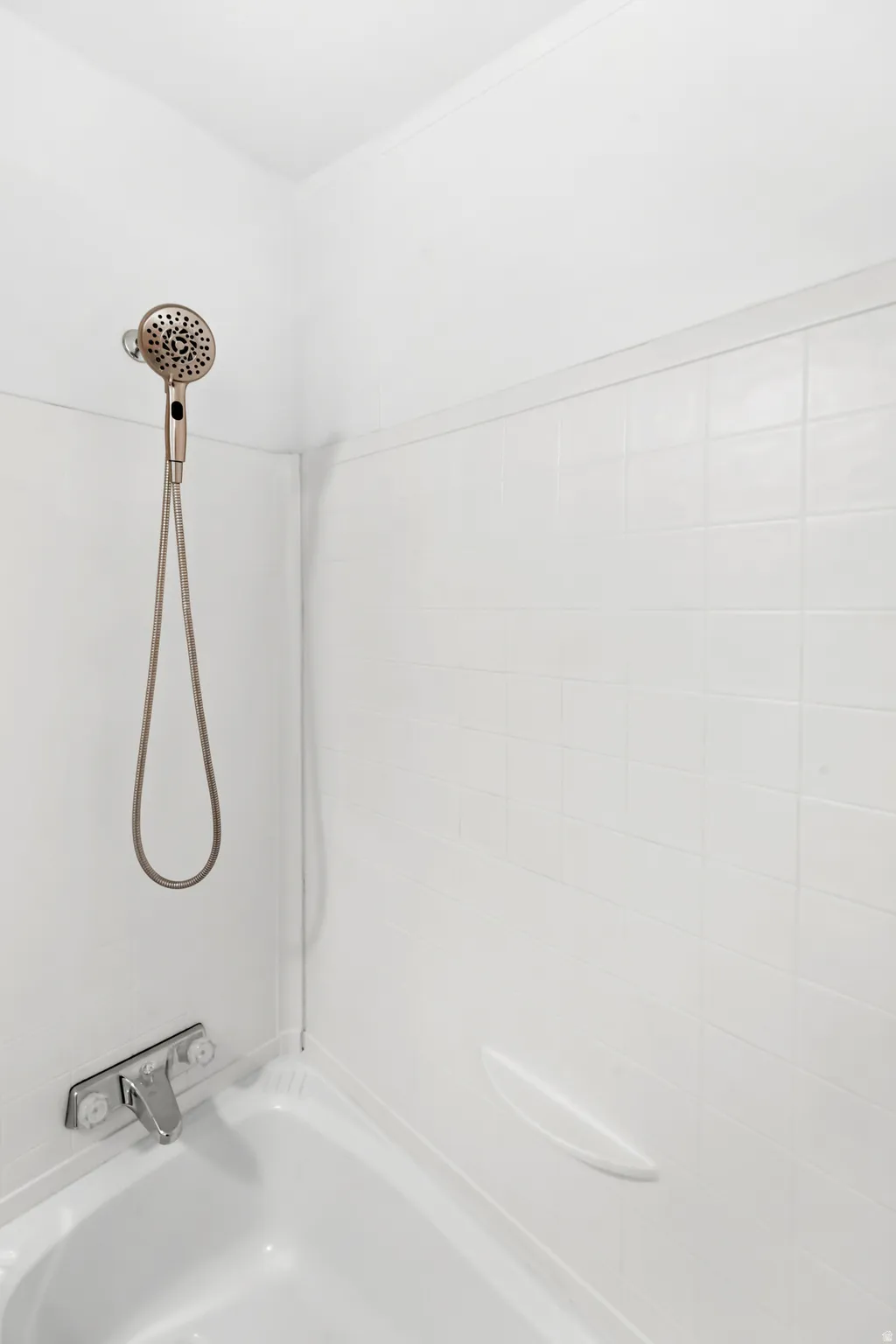 Bathtub and shower combination featuring white tiled walls and a handheld shower fixture