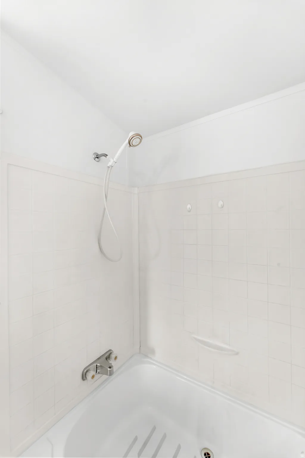 White tiled shower enclosure with a hand-held showerhead and built-in soap dishes
