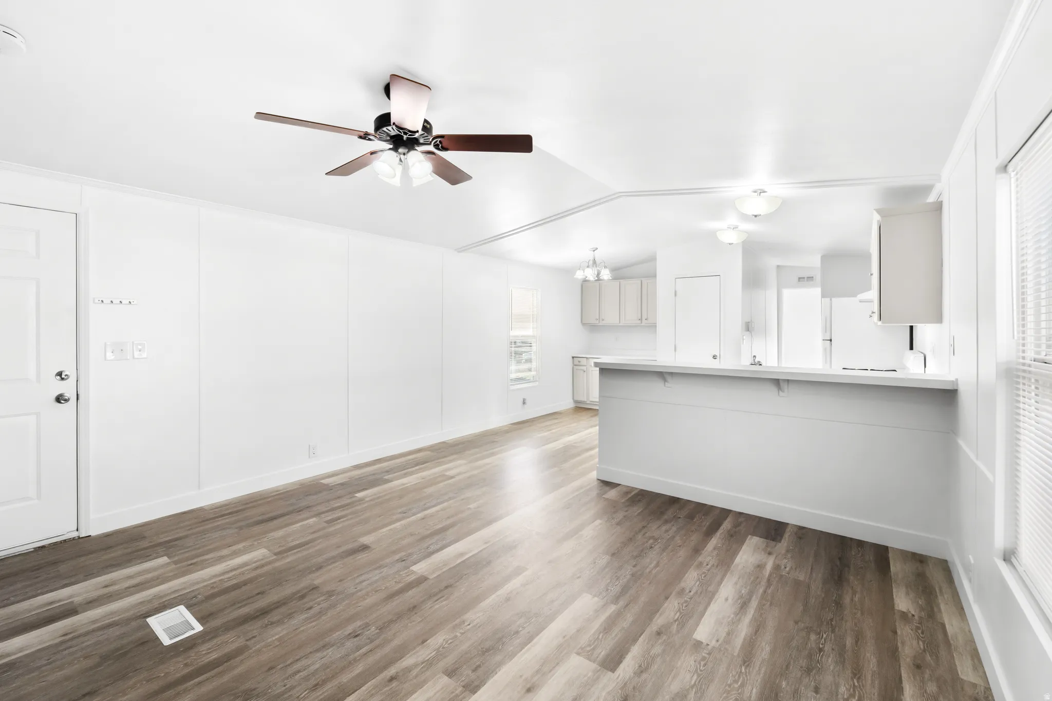 Living area featuring wood-finish flooring, white panel walls, and a ceiling fan